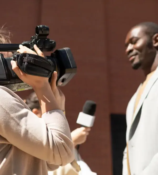 african-man-in-gray-suit-taking-video-interview-with-camera-crew